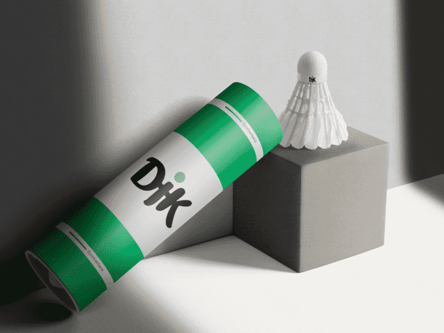 Verpackung eines Badmintonschl&auml;gers steht neben einem Badmintonball auf einem grauen Block. Licht f&auml;llt auf die Szene.