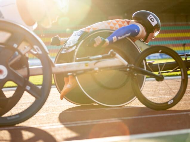 Nahaufnahme zweier Rennrollst&uuml;hle auf der Laufbahn, w&auml;hrend Sportler im Wettkampf um die Wette fahren.