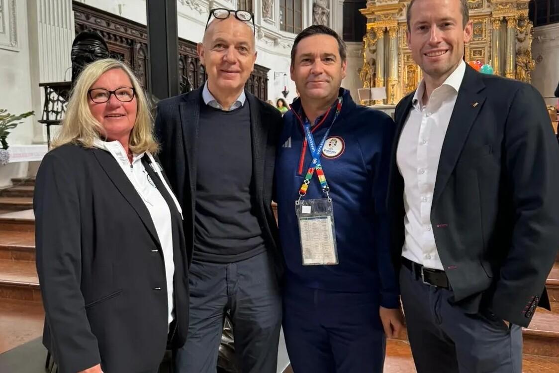 Vier Personen posieren in einer Kirche vor einem kunstvollen Altar. Helle, historische Architektur im Hintergrund.