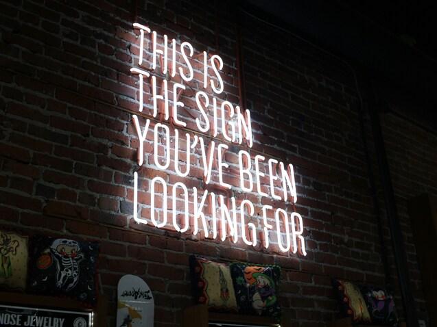 Neonlicht mit der Aufschrift „THIS IS THE SIGN YOU'VE BEEN LOOKING FOR“ an einer Ziegelwand.