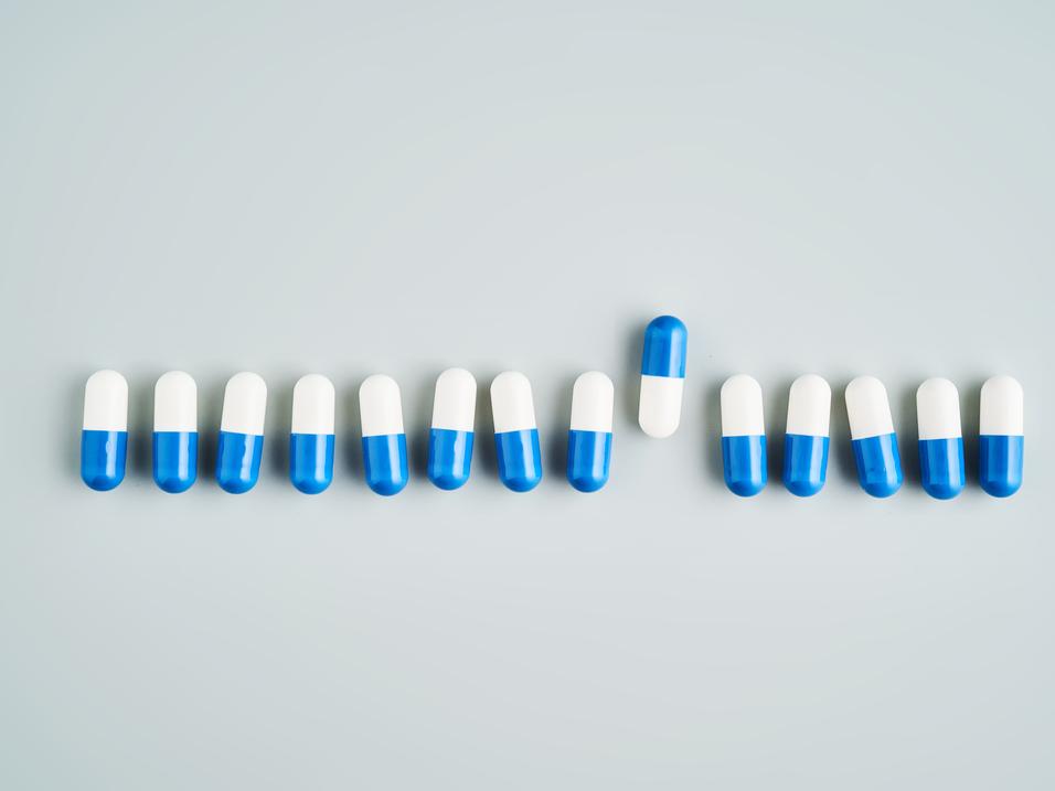 Reihe blauer und wei&szlig;er Kapseln auf grauem Hintergrund, eine Kapsel hebt sich aus der Anordnung hervor.
