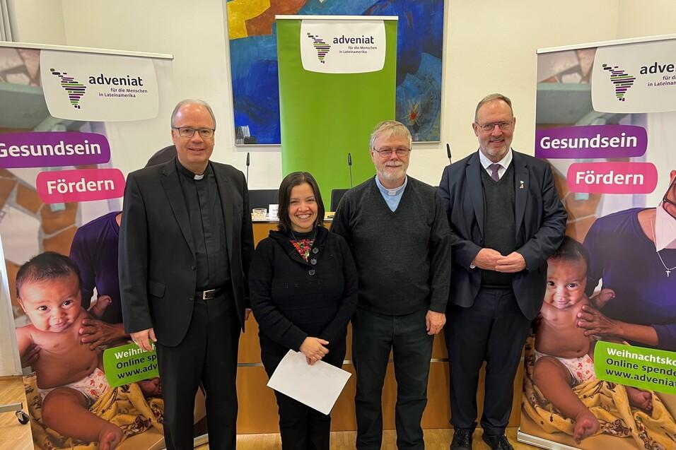 Vier Personen stehen vor Bannern von Adveniat, die das Thema Gesundheit f&ouml;rdern. Sie l&auml;cheln freundlich in die Kamera.