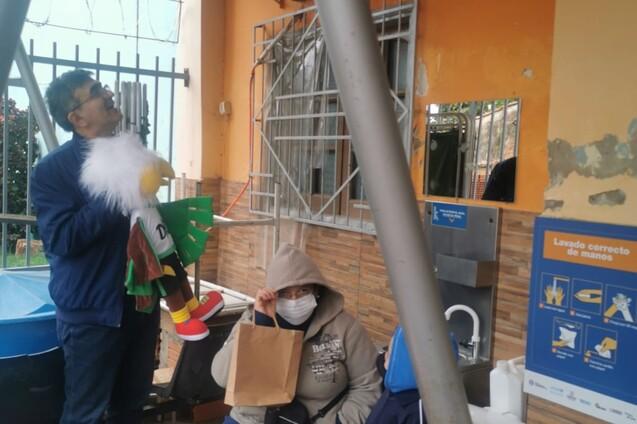 Personen in einem Warteraum vor gesundheitlicher Einrichtung mit Hinweisschild, einer Person h&auml;lt ein Spielzeug.