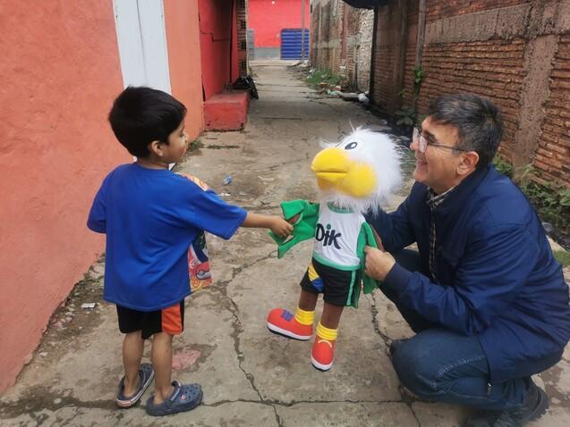 Junge interagiert mit einem Erwachsenen und einem pl&uuml;schigen Maskottchen in einer schmalen Gasse.
