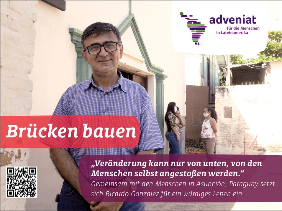 Mann mit Brille steht vor einer Wand und h&auml;lt ein Schild mit dem Text &bdquo;Br&uuml;cken bauen&ldquo; in Asunci&oacute;n, Paraguay.