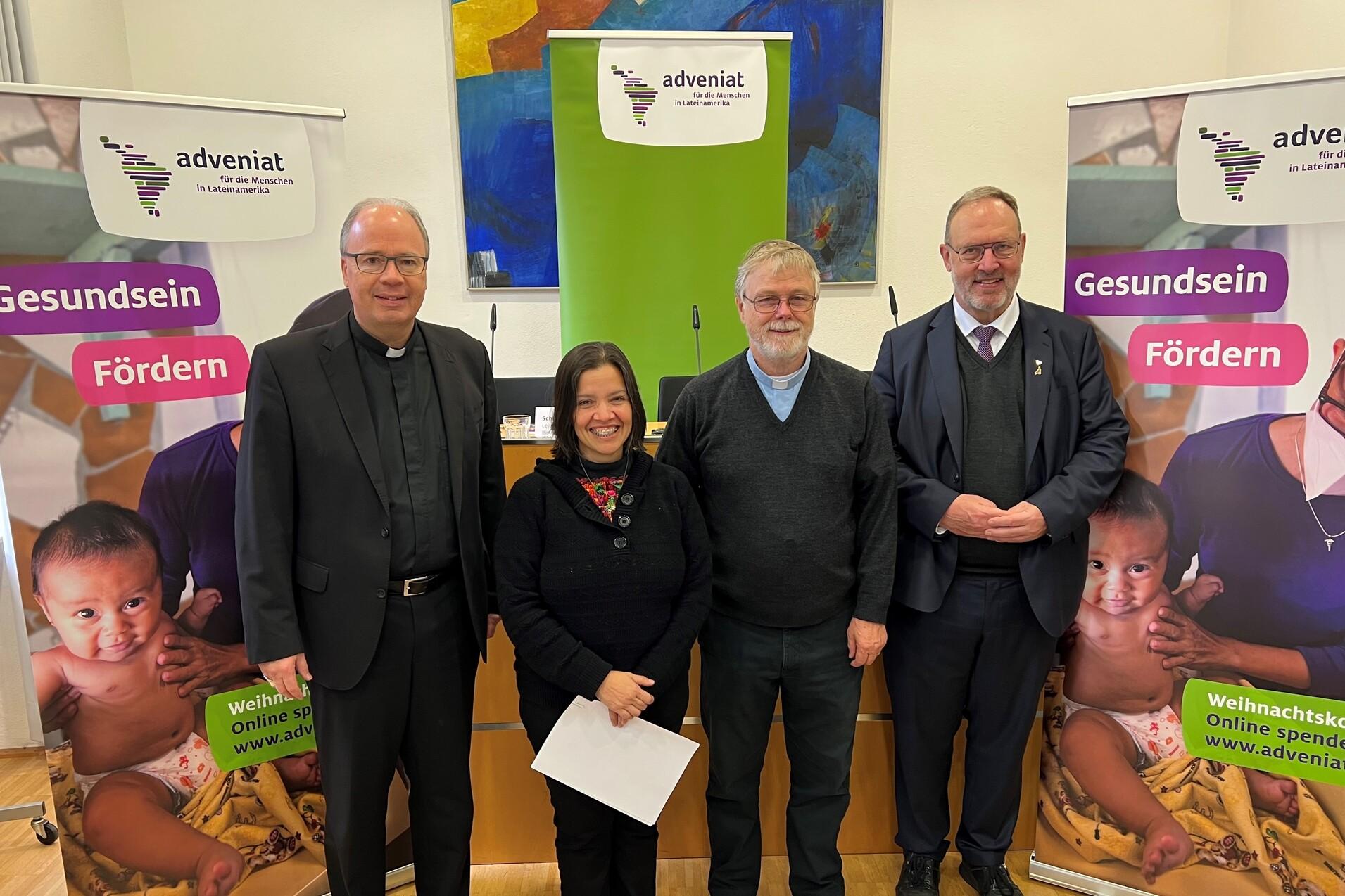 Vier Personen stehen vor Bannern von Adveniat, die das Thema Gesundheit f&ouml;rdern. Sie l&auml;cheln freundlich in die Kamera.