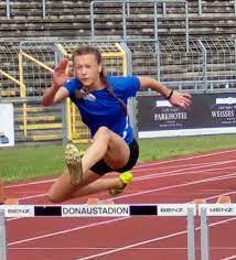 Junge Athletin springt &uuml;ber eine H&uuml;rde auf einer Tartanbahn im Donaustadion.