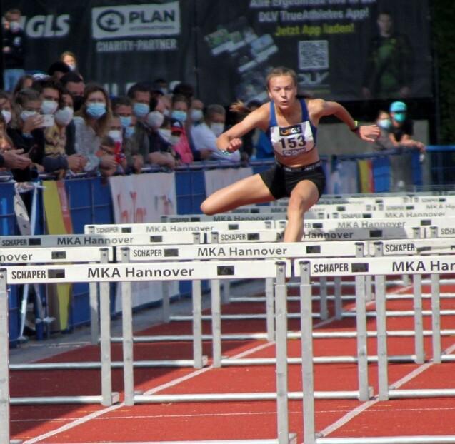 Junge Athletin springt &uuml;ber H&uuml;rden bei einem Leichtathletik-Event in Hannover, Zuschauer im Hintergrund.