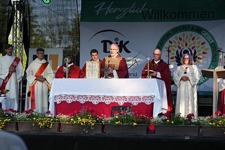 Eine Gruppe von f&uuml;nf Personen in liturgischer Kleidung steht an einem festlich gedeckten Altar auf einer B&uuml;hne.