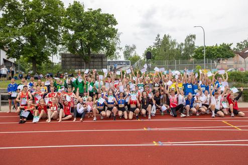 Gruppierung von Athleten in verschiedenen Trikots, die jubelnd auf einer Laufbahn stehen und kleine Papiere halten.