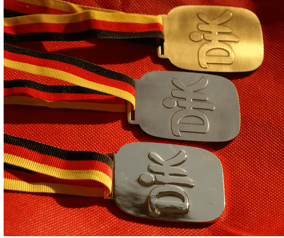 Drei Medaillen mit dem Wort "Dik" und Deutschland-Farben an den B&auml;ndern liegen auf einem roten Untergrund.