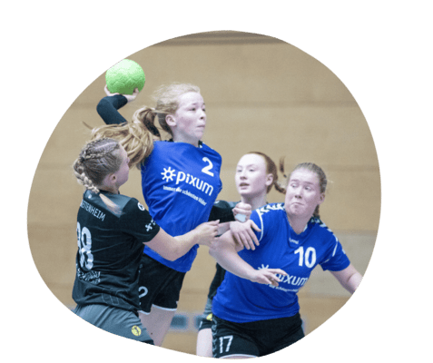 Handballspiel mit Spielerinnen in Aktion, eine wirft den Ball, w&auml;hrend andere um den Ball k&auml;mpfen.