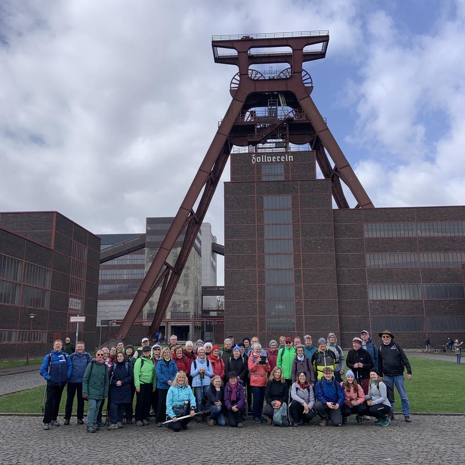 Gruppenfoto von rund 40 Menschen vor der imposanten F&ouml;rderanlage der Zeche Zollverein an einem bew&ouml;lkten Tag.