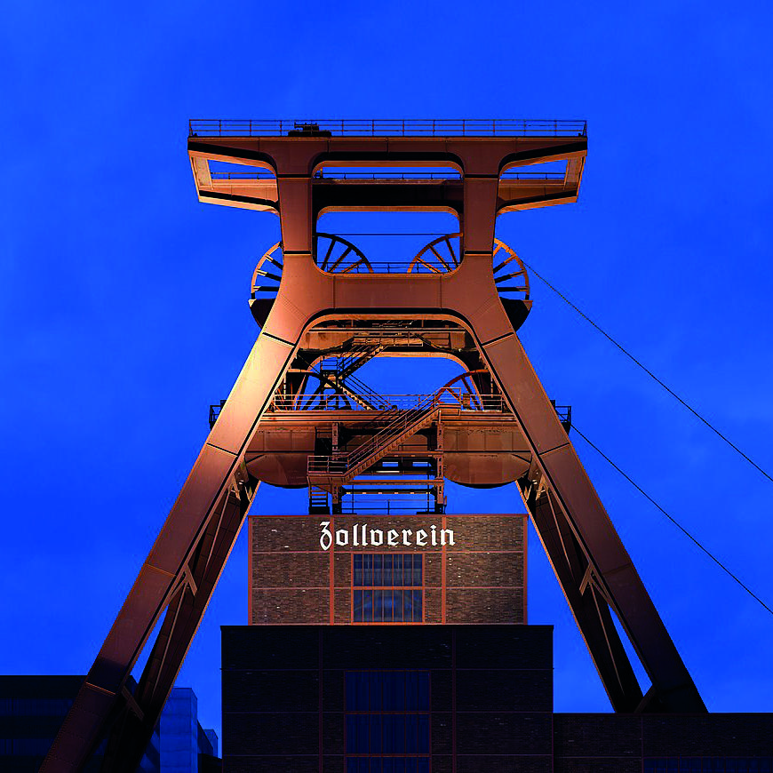 Detailaufnahme des F&ouml;rderturms des UNESCO-Weltkulturerbes Zollverein bei D&auml;mmerung, vor blauem Himmel.