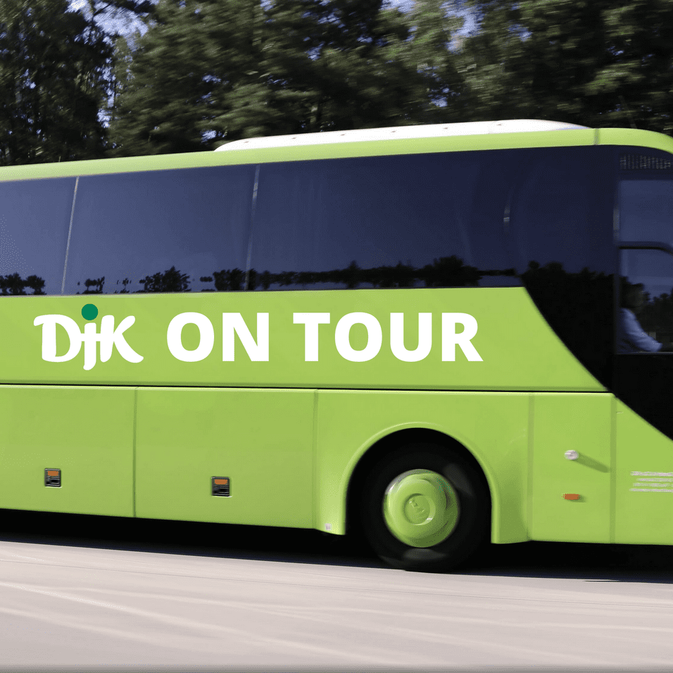 Gr&uuml;ner Reisebus mit der Aufschrift &bdquo;DJK ON TOUR&ldquo; f&auml;hrt auf einer Stra&szlig;e, umgeben von B&auml;umen.