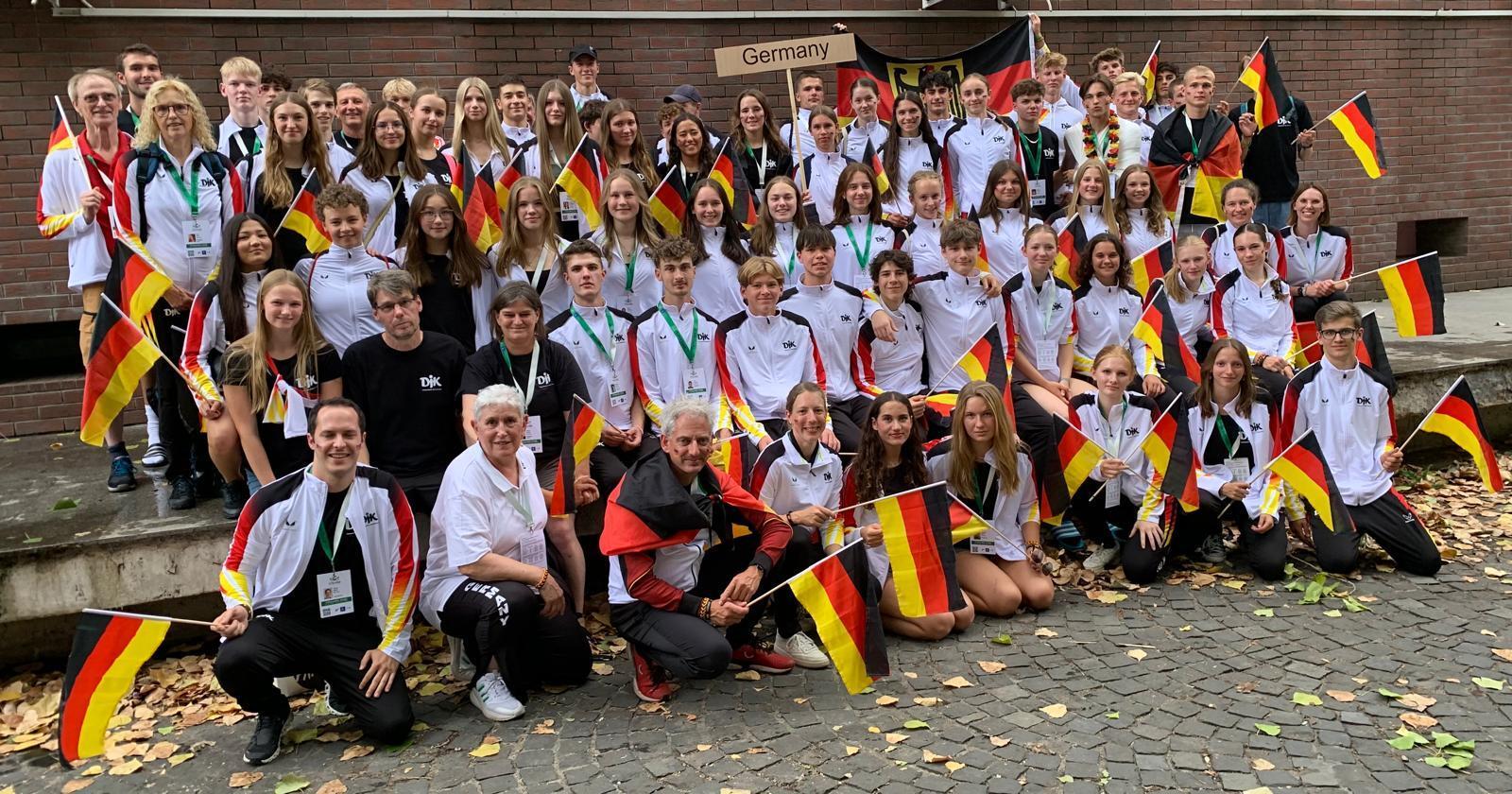 Gruppennahaufnahme von 60 Teilnehmern in Sportbekleidung, die stolz kleine Deutschlandflaggen halten.