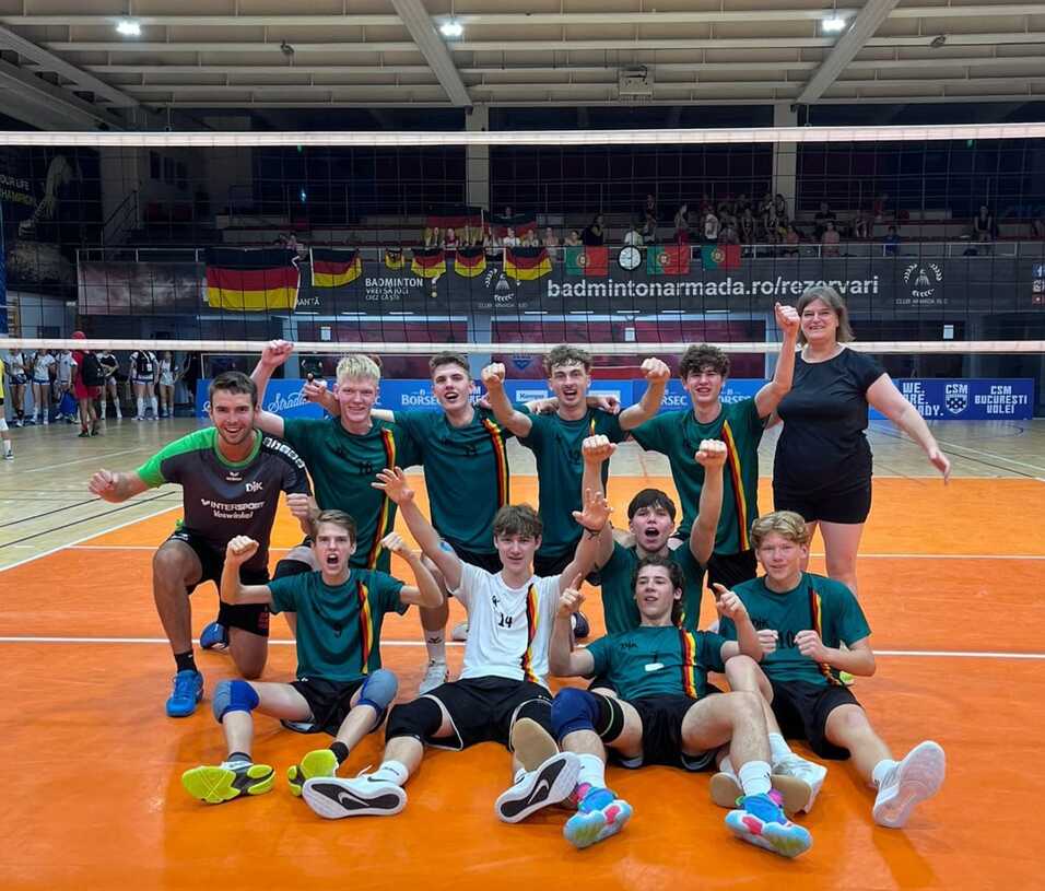 Gruppenselfie von zw&ouml;lf Volleyballspielern in Turnier-T-Shirts, l&auml;chelnd auf dem Spielfeld posierend.