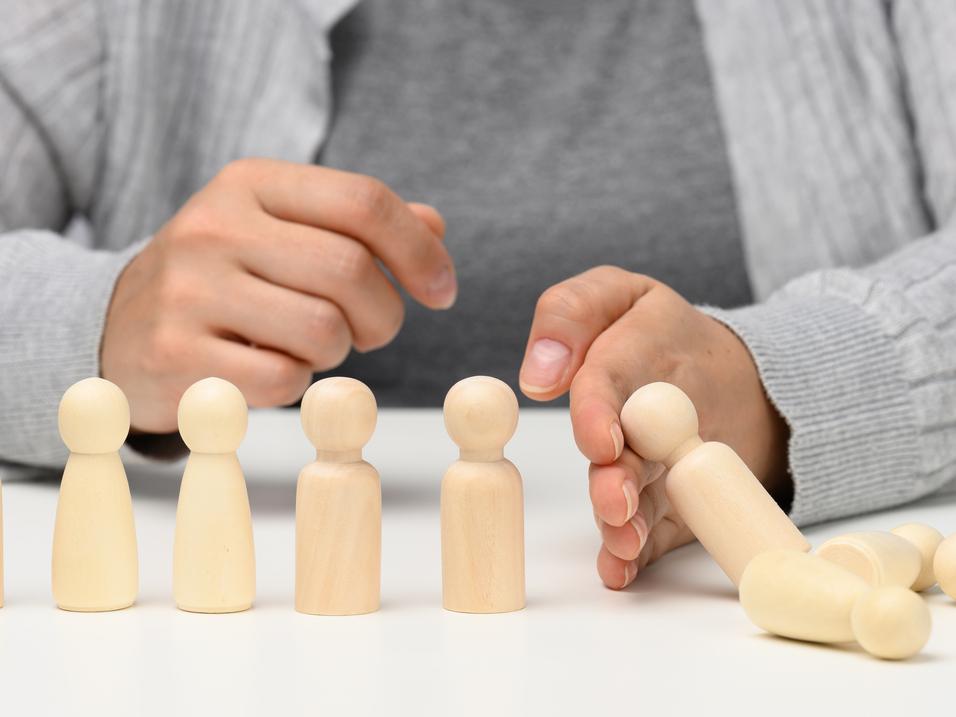 H&auml;nde platzieren eine Holzfigur neben weiteren Figuren auf einem Tisch. Eine Figur liegt bereits umgekippt.