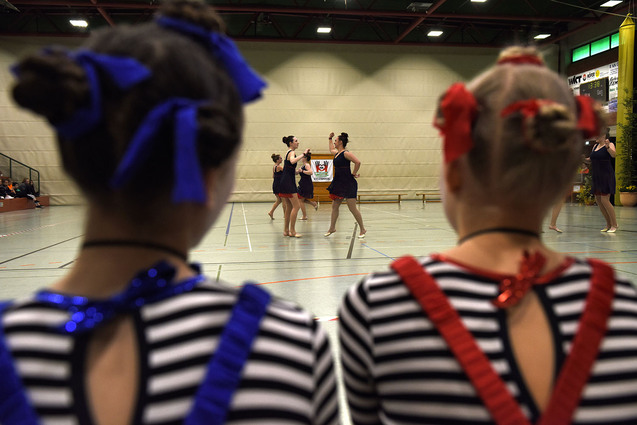 Zwei M&auml;dchen mit bunten Haarknoten beobachten T&auml;nzerinnen in einem Sportzentrum w&auml;hrend einer Auff&uuml;hrung.