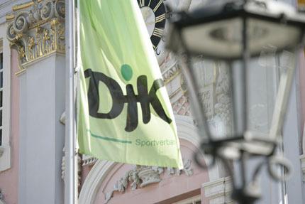 Grüne Fahne mit dem Schriftzug „DJK Sportverband“ vor einem historisch gestalteten Gebäude und einer Laterne.