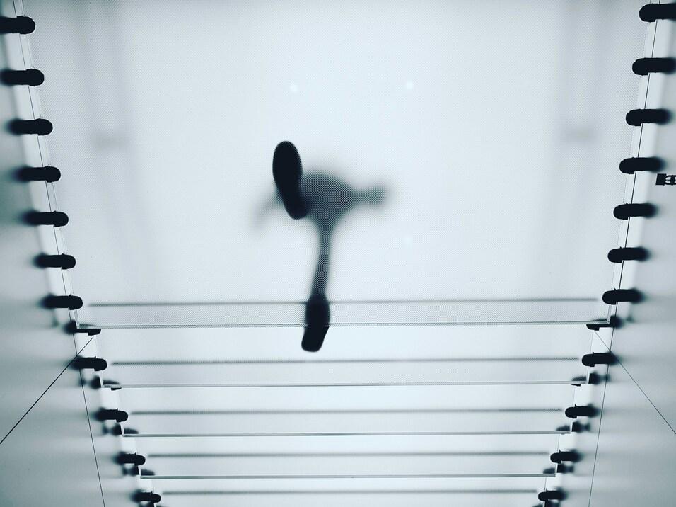 Sicht von unten auf eine Fu&szlig;g&auml;ngerfigur, die &uuml;ber transparente Stufen in einem modernen Geb&auml;ude schreitet.