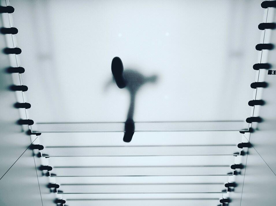 Sicht von unten auf eine Fu&szlig;g&auml;ngerfigur, die &uuml;ber transparente Stufen in einem modernen Geb&auml;ude schreitet.