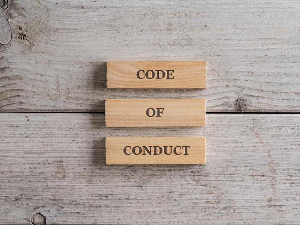 Drei Holzpl&auml;ttchen mit der Aufschrift &bdquo;CODE&ldquo;, &bdquo;OF&ldquo; und &bdquo;CONDUCT&ldquo; auf einer grauen Holzoberfl&auml;che.