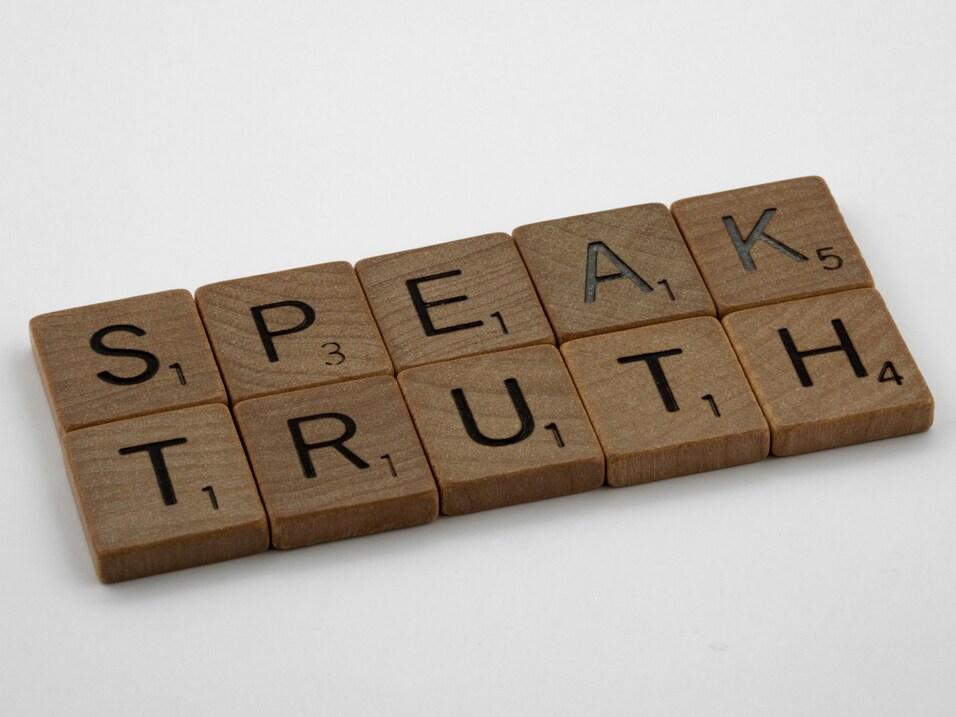 Holzbuchstaben auf einem wei&szlig;en Hintergrund spellend &bdquo;SPEAK TRUTH&ldquo;.