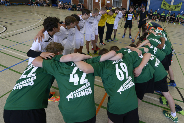 Zwei Gruppen von Jugendspielern in Sportanz&uuml;gen bilden einen Kreis in einer Sporthalle und bereiten sich auf ein Spiel vor.