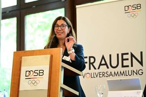 Frau spricht am Rednerpult bei der Frauen-Vollversammlung des DOSB, im Hintergrund das Banner mit dem Logo.