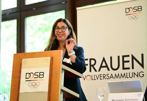 Frau spricht am Rednerpult bei der Frauen-Vollversammlung des DOSB, im Hintergrund das Banner mit dem Logo.