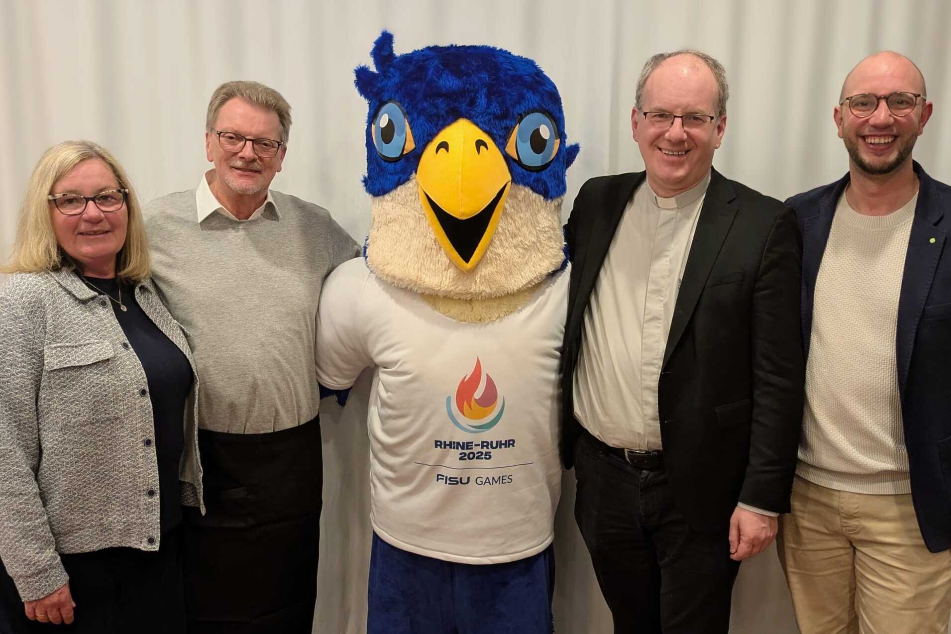 Vier Personen und ein Maskottchen mit blauer M&uuml;tze und gelbem Schnabel stehen vor einem wei&szlig;en Hintergrund.
