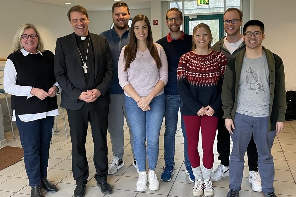 Gruppenfoto mit acht Personen in einem Foyer, darunter ein Pfarrer, Frauen und M&auml;nner in Freizeitkleidung.