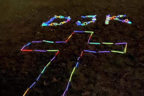 Leuchtende bunte Materialien formen ein Kreuz und die Buchstaben &bdquo;DJK&ldquo; auf dem Boden im Dunkeln.