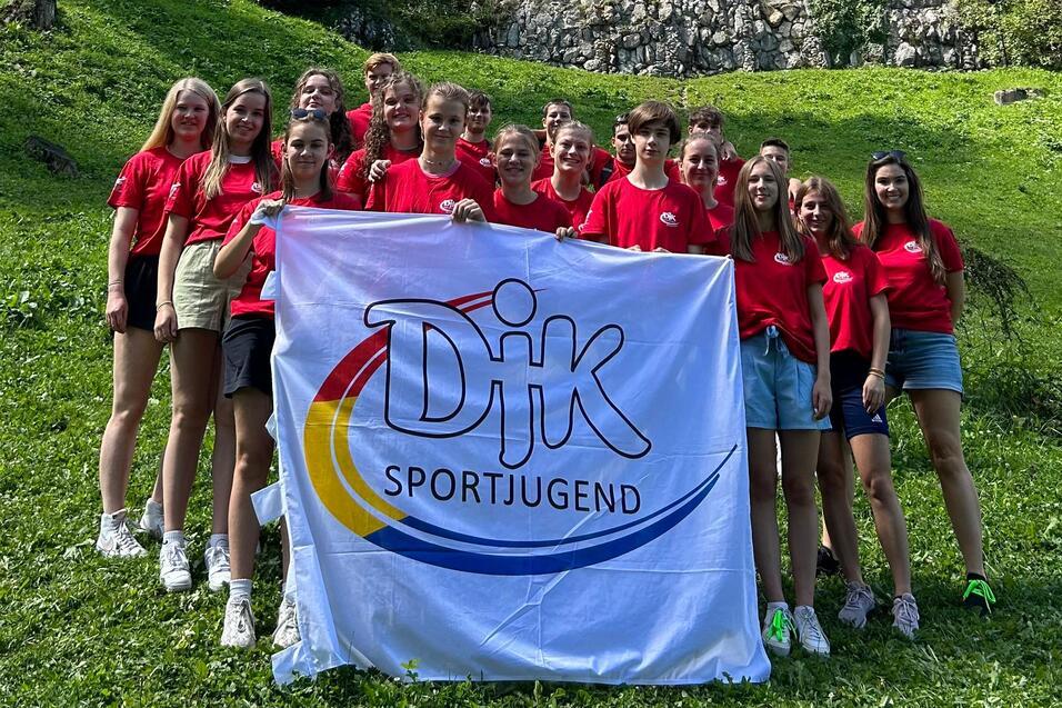 Gruppe junger Menschen in roten T-Shirts posiert mit einer Flagge vor einer Burg auf einem Hang.
