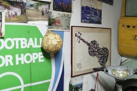 Wand mit Plakaten, Fotos und einem Fu&szlig;ball; daneben ein gerahmtes Bild einer Gitarre und alte Gegenst&auml;nde.