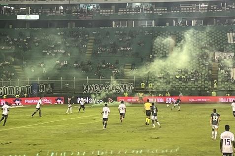 Fu&szlig;ballspiel auf einem Stadionfeld mit Spielern und rauchigen Effekten, leere Zuschauertrib&uuml;nen im Hintergrund.