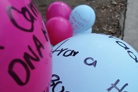 Bunte Luftballons in Pink und Blau, beschriftet mit verschiedenen Texten, liegen auf dem Boden.