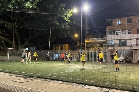 F&uuml;nf Personen in Sportkleidung spielen Fu&szlig;ball auf einem beleuchteten Kunstrasenplatz nachts.