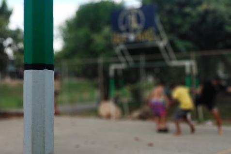 Nahaufnahme eines gr&uuml;nen Basketballkorb-Pfostens auf einem Sportplatz mit spielenden Kindern im Hintergrund.