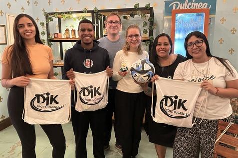 Sechs Personen l&auml;cheln, halten Baumwolltaschen mit Aufdruck &bdquo;DJK Sportjugend&ldquo; und einen Fu&szlig;ball in einem gem&uuml;tlichen Raum.