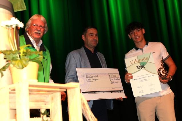 Drei Personen auf einer B&uuml;hne halten eine Urkunde und einen Scheck zur Preisverleihung in den H&auml;nden.