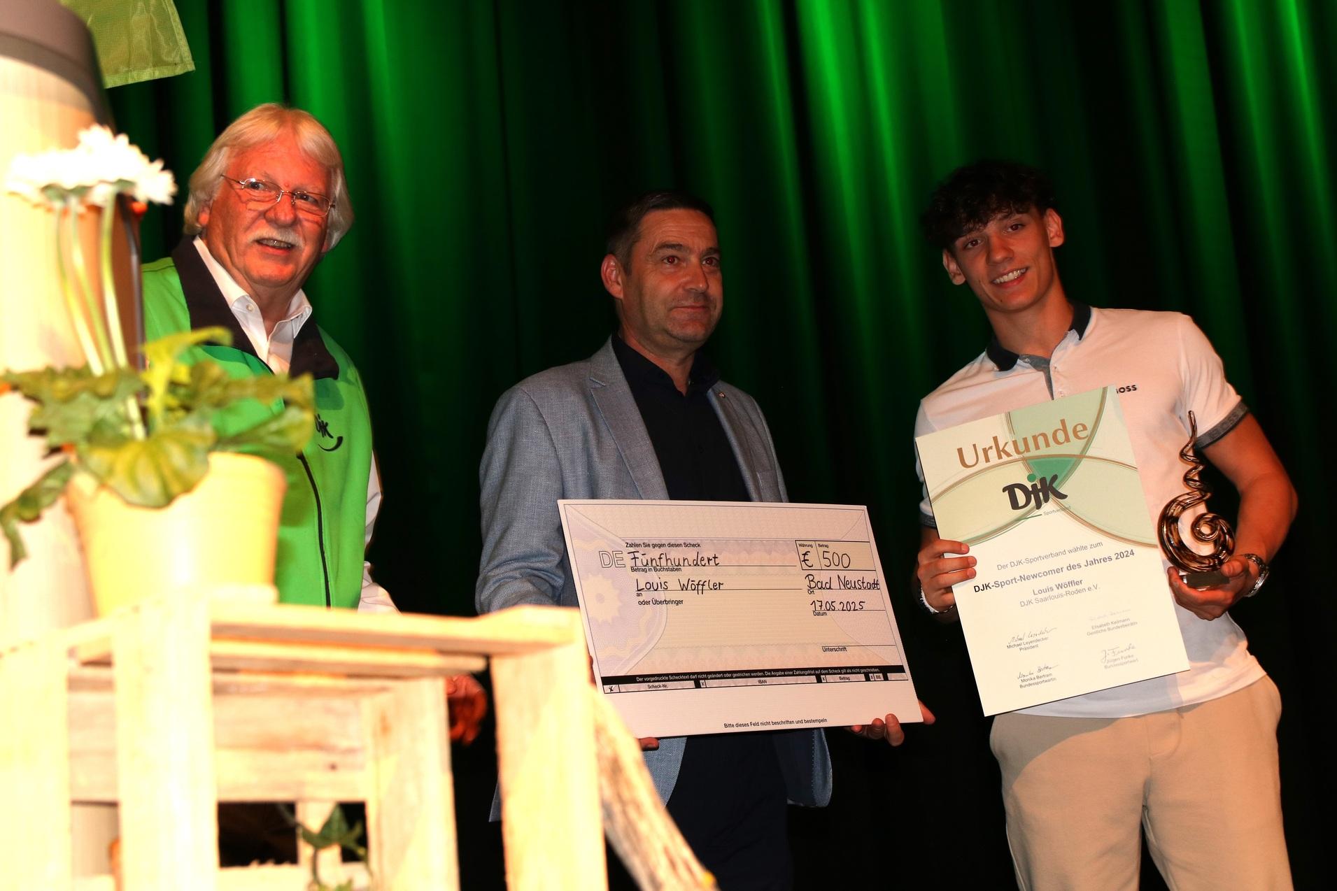 Drei Personen auf einer B&uuml;hne halten eine Urkunde und einen Scheck zur Preisverleihung in den H&auml;nden.