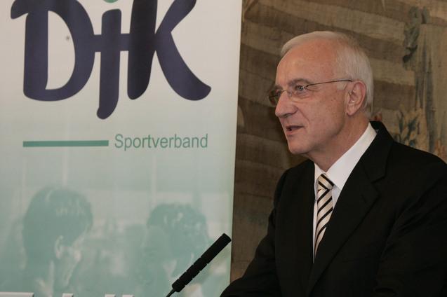 Mann im Anzug spricht an einem Rednerpult vor einem Banner des DJK-Sportverbands.