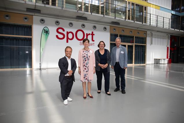Vier Personen stehen in einem modernen Raum mit dem Schriftzug &bdquo;SpOrt Stuttgart&ldquo; im Hintergrund.