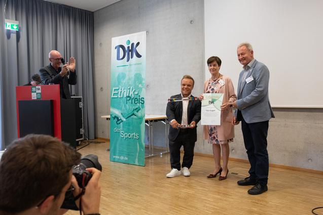 Drei Personen stehen auf einer B&uuml;hne und halten eine Urkunde f&uuml;r den Ethik-Preis des Sports in den H&auml;nden.