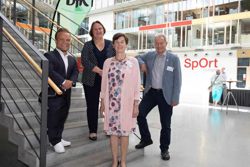 Vier Personen stehen auf einer Treppe in einem modernen Geb&auml;ude. Hintergrund mit "SpOrt" Schriftzug.