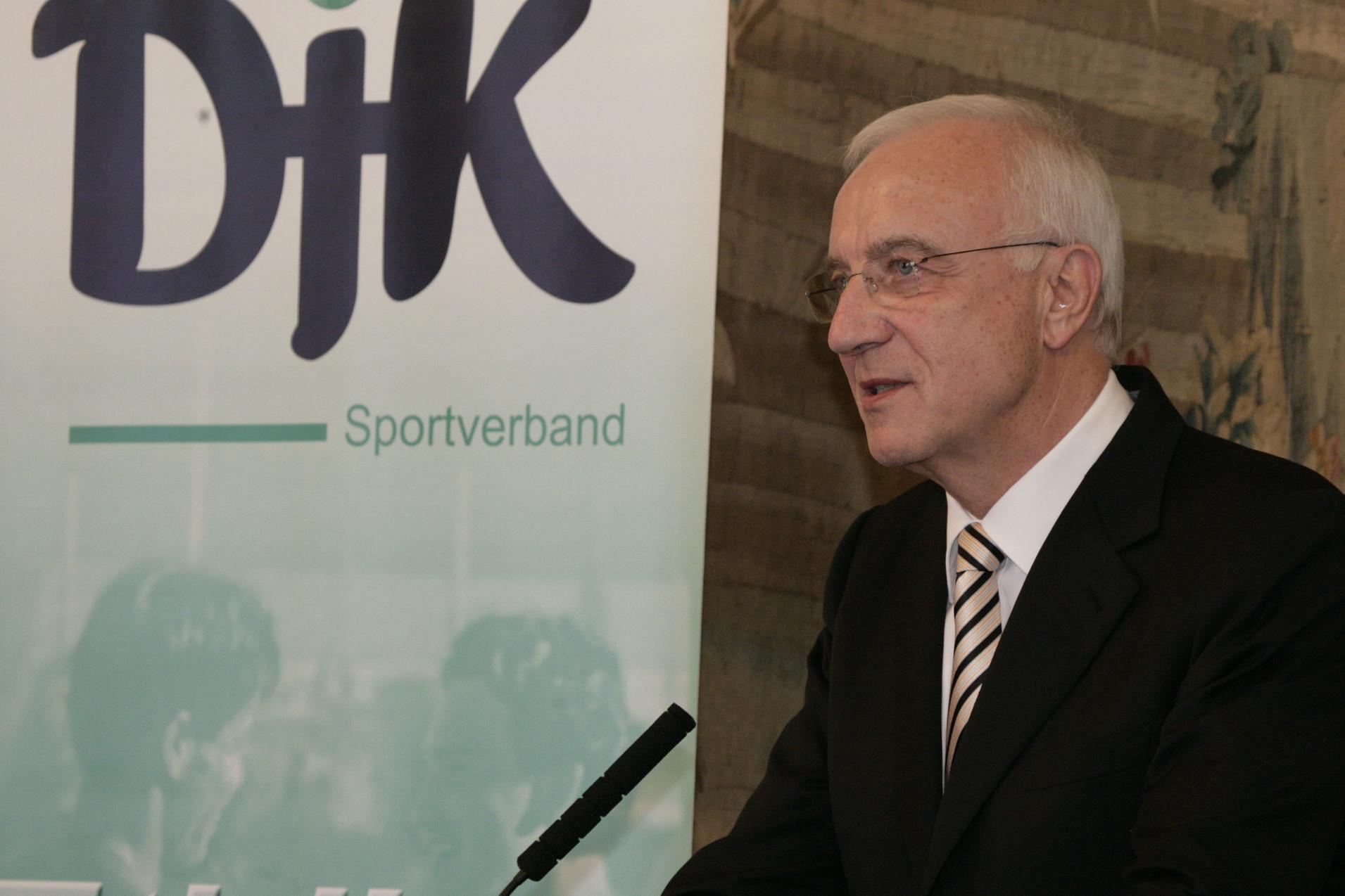Mann im Anzug spricht an einem Rednerpult vor einem Banner des DJK-Sportverbands.