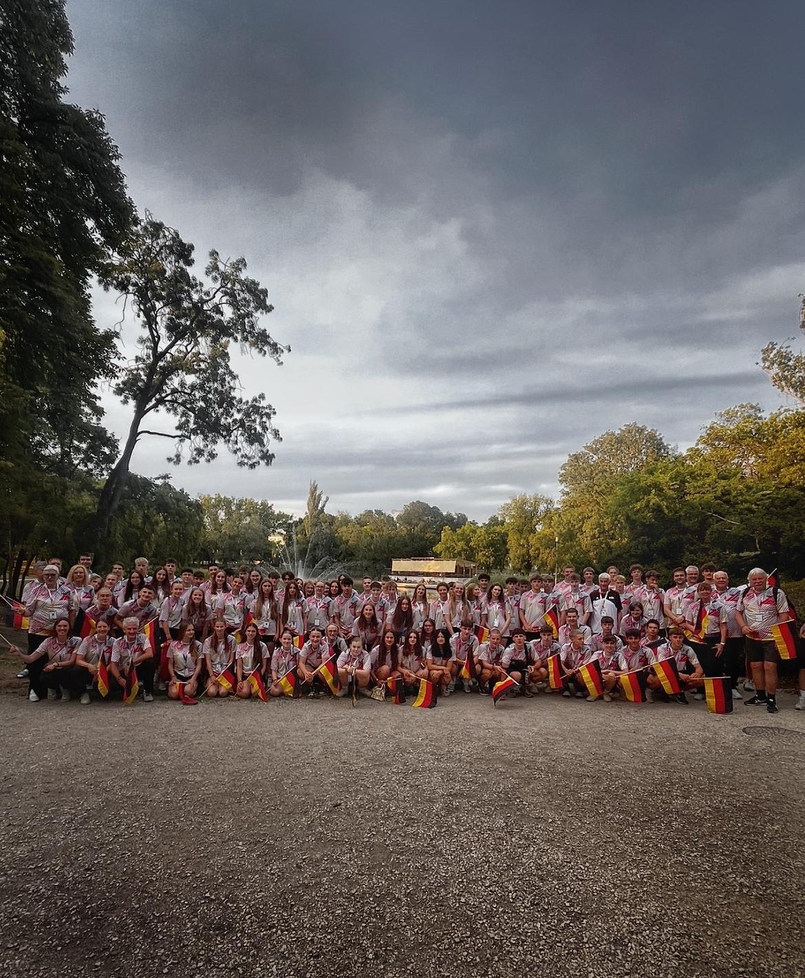 Gruppenfoto von mehr als 100 Personen in einem Park, die einheitliche T-Shirts tragen und mit Fahnen posieren.