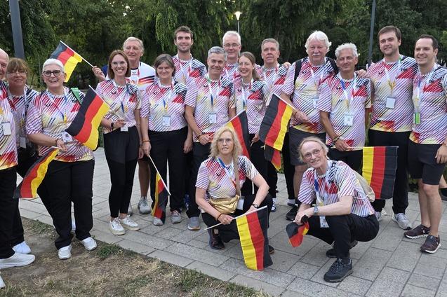 Gruppe von Menschen in bunten Shirts in Veranstaltung, posierend mit kleinen Deutschlandflaggen im Freien.